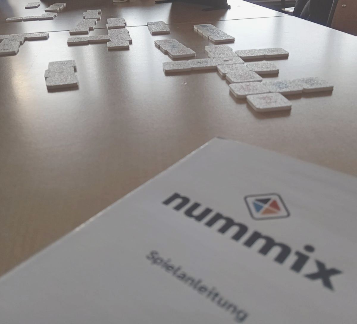 Die nummix-Spielanleitung auf dem Tisch, dahinter Steine